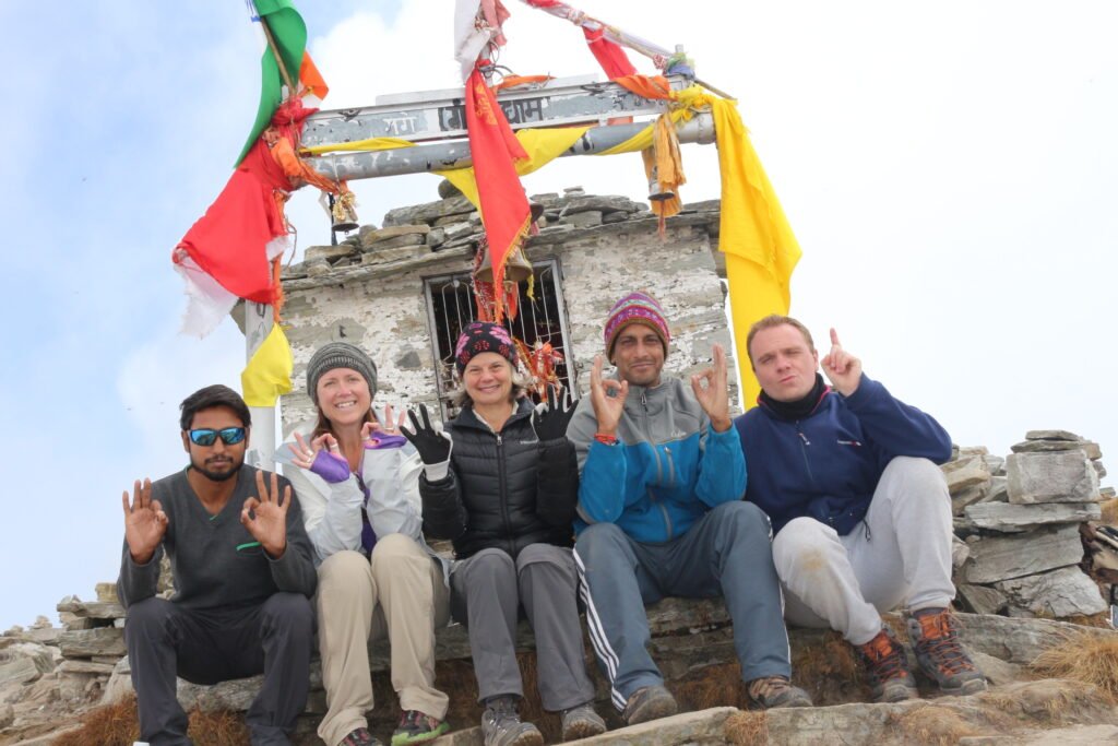 Trekkers smiling under prayer flags on the Chandrashila trek in Uttarakhand